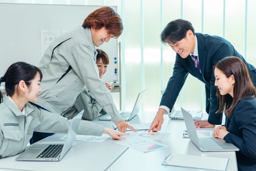 会議で資料を指差す男性(作業着とスーツ)