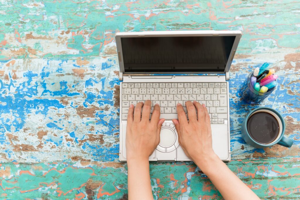 デスクの上のノートパソコンをタイピングする手と文具とコーヒー